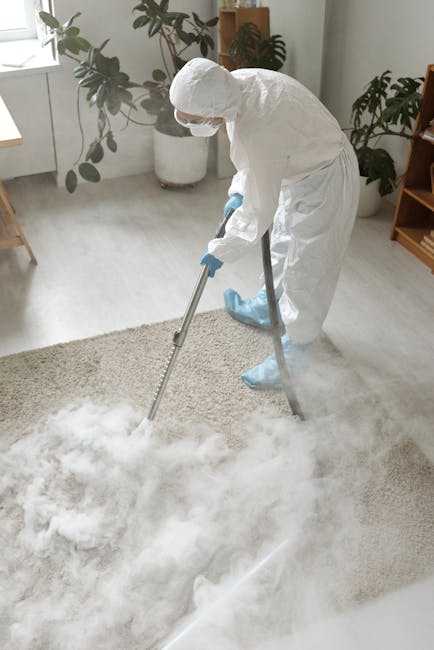 A person operating a yellow vacuum cleaner on an ornate patterned rug in a living room, with wooden flooring nearby and a brown leather sofa partially visible. The individual is dressed casually and appears to be performing surface cleaning to remove dust and dirt from the carpet. Natural light illuminates the room, highlighting the cleanliness of the rug and surrounding area. This scene exemplifies professional deep cleaning, with a focus on maintaining hygiene and enhancing the appearance of domestic surfaces, as provided by Brent Carpet Cleaning, a specialist in cleaning services for residential and commercial spaces.